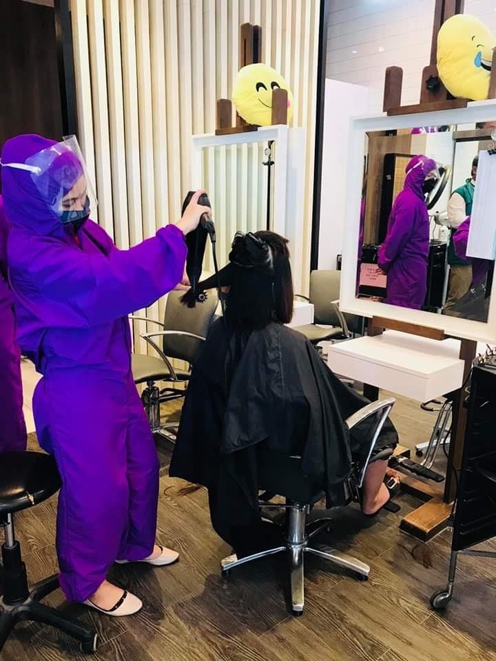 A salon worker, wearing a purple PPE, servicing a client in a salon  in a mall in Region 9