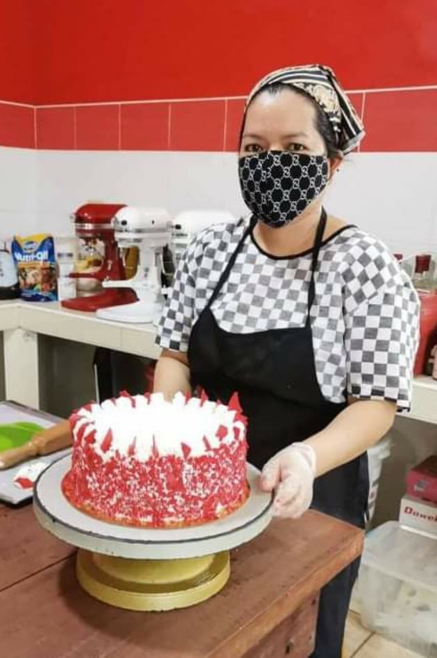 Erlynn in kitchen wear, standing over a freshly baked cake