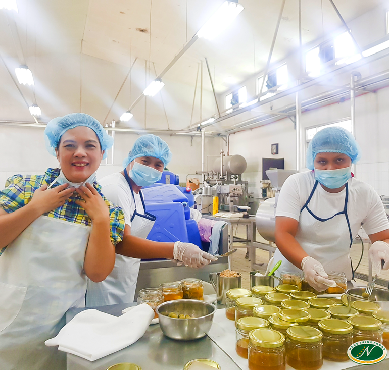  Nene Prime Foods employees leaning over a table full of bottled olive oil, ready to pack them with bangus flakes